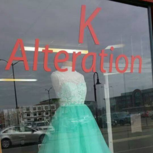 Image of store window with the words K Alteration in red font on it. Behind the glass is a green blue prom dress on a mannequin. This is one of the Asian businesses that won an award in Chippewa Valley.